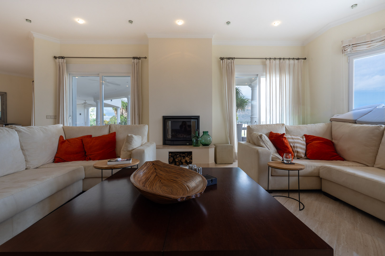 Helles Wohnzimmer mit zentralem Kamin, cremefarbenen Sofas und direktem Zugang zur Terrasse durch große Glasschiebetüren.