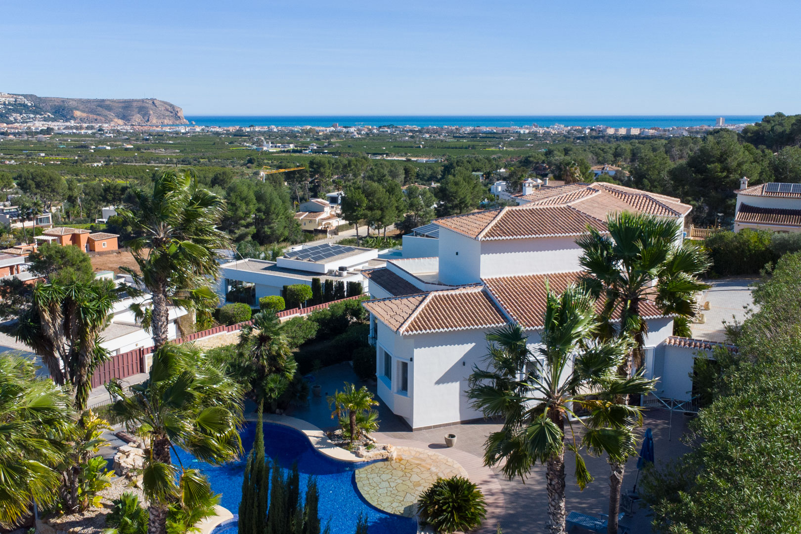 Luftaufnahme der weißen Villa mit Pool, umgeben von Palmen und mit weitem Panoramablick auf das Mittelmeer und die Küste.