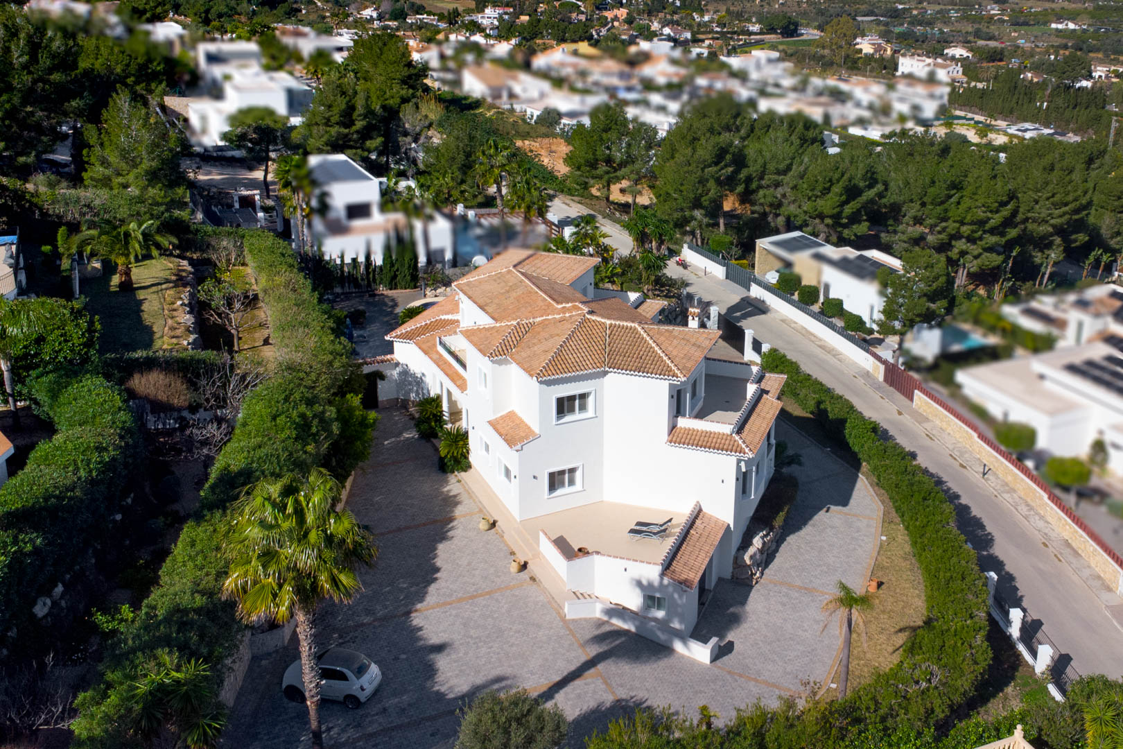 Luftaufnahme der weißen Villa mit traditionellem Ziegeldach, großzügig gepflasterter Einfahrt und privaten Terrassen inmitten mediterraner Bepflanzung.