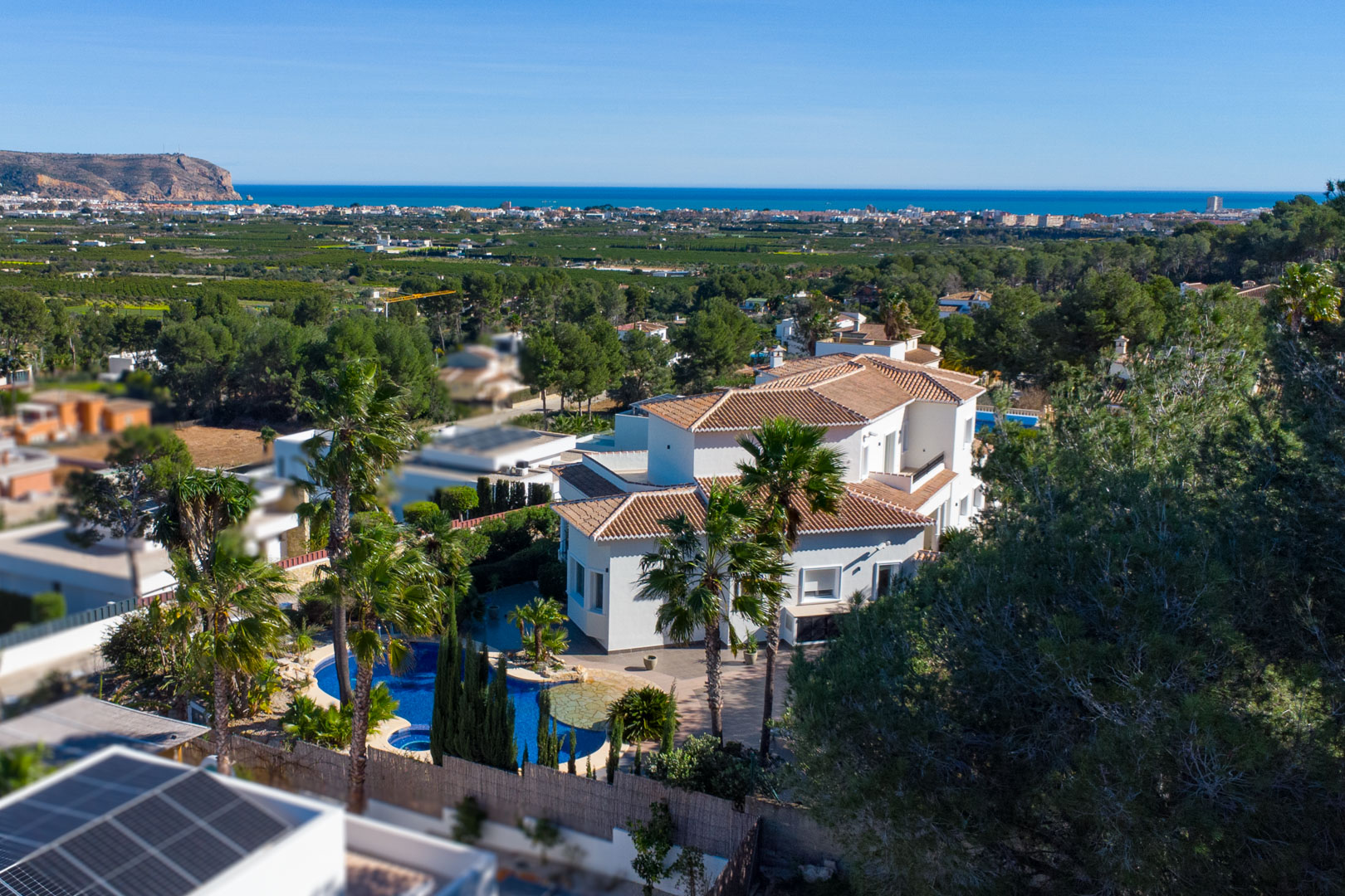 Luftaufnahme der weißen Villa mit Ziegeldächern, privatem Pool und Jacuzzi, umgeben von Palmen mit weitem Blick auf die Mittelmeerküste und das Meer.