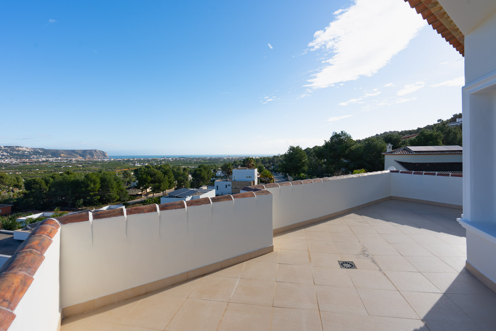 Obere Terrasse mit beigen Keramikfliesen und gemauerter Brüstung, die einen Panoramablick auf das Mittelmeer und die umliegende Tallandschaft bietet.