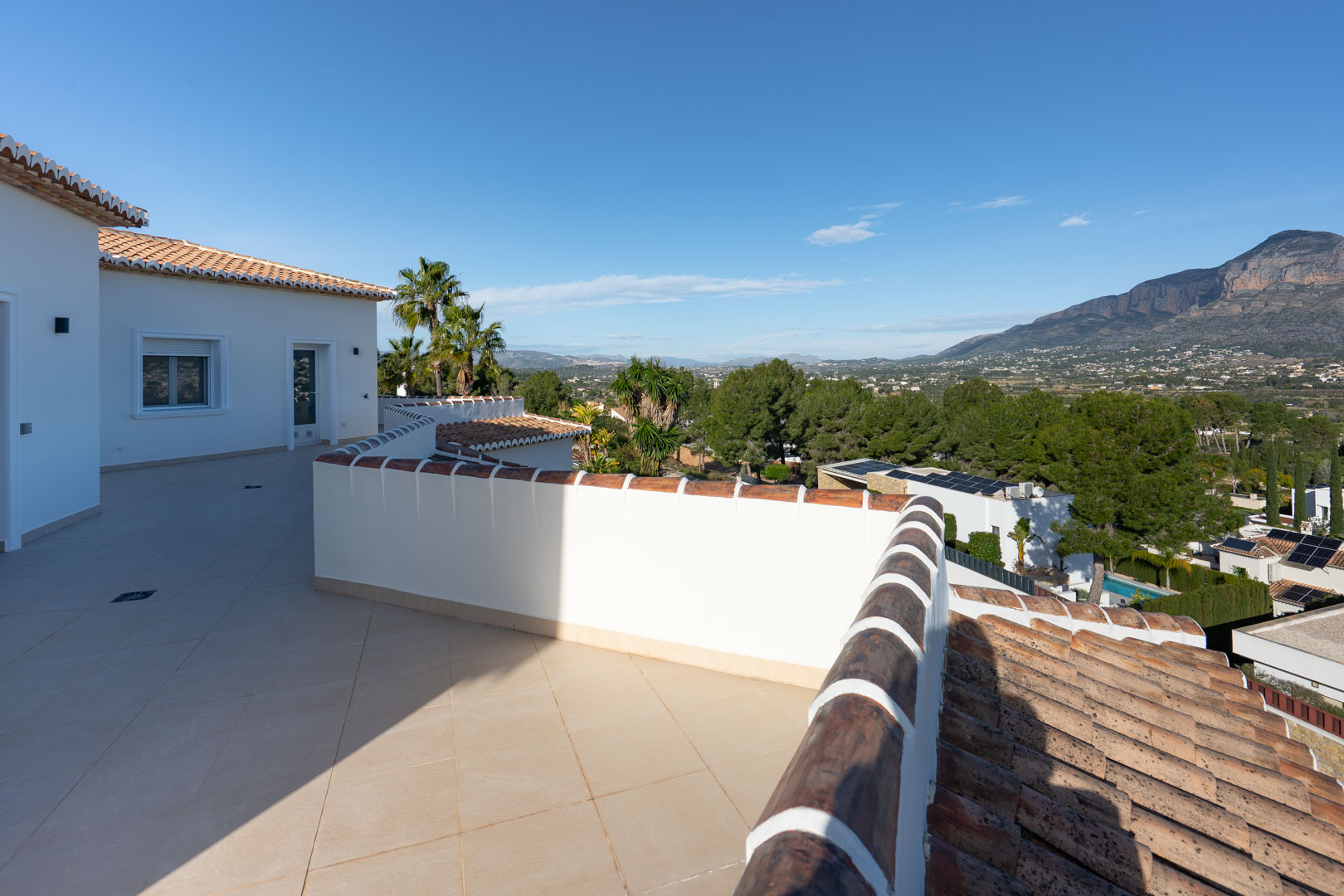 Obere Terrasse mit sandfarbenen Keramikfliesen und Panoramablick auf das Montgó-Massiv und die umliegende mediterrane Landschaft.