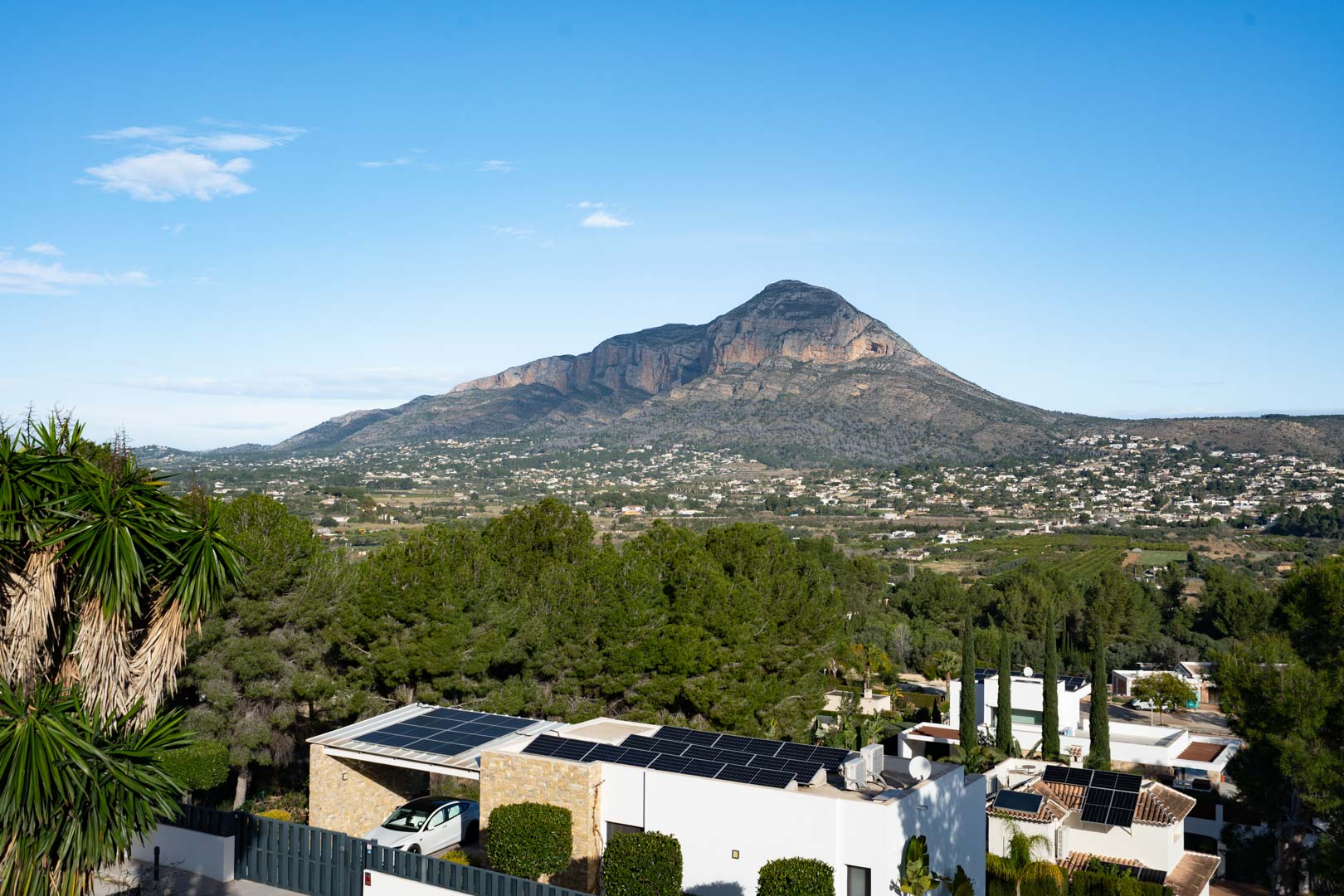 Panoramablick auf das Montgó-Massiv vom Anwesen aus, mit Fokus auf die Solaranlage auf dem Dach und die in die mediterrane Pinienlandschaft eingebettete Wohngegend.