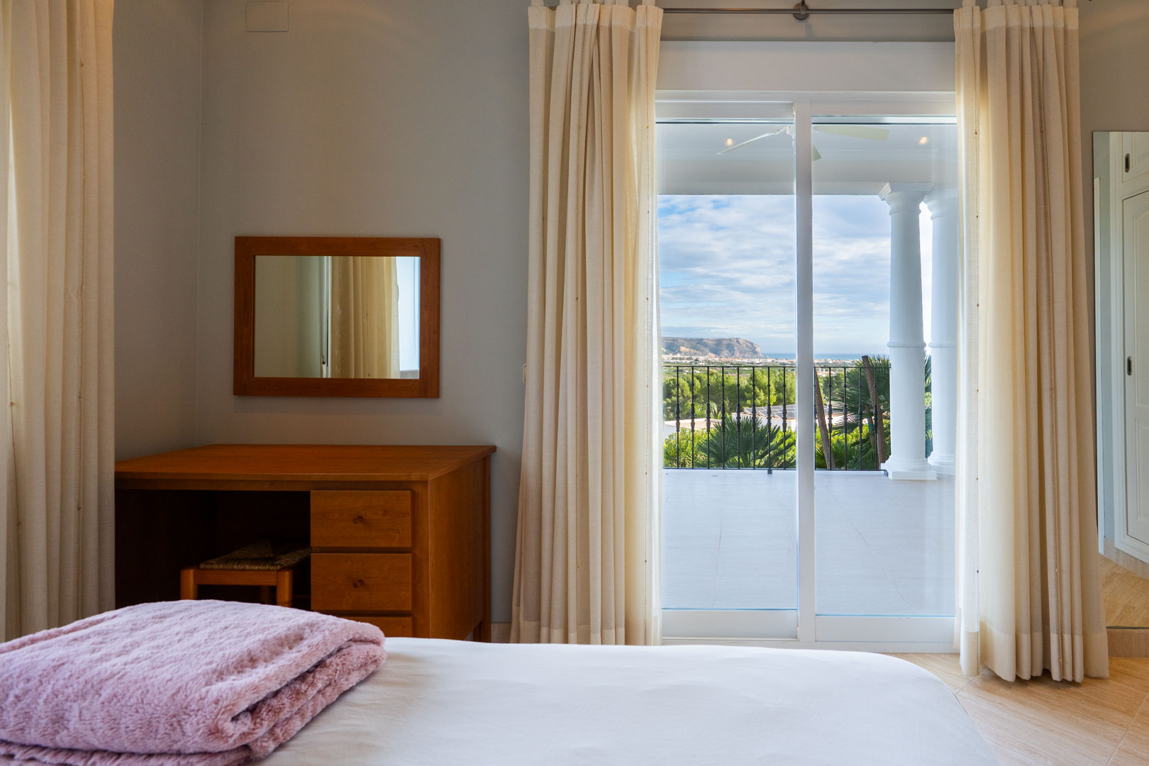 Schlafzimmer mit Holzschreibtisch und direktem Zugang zur privaten Terrasse mit weißen Säulen und Blick auf das Meer und den Montgó.