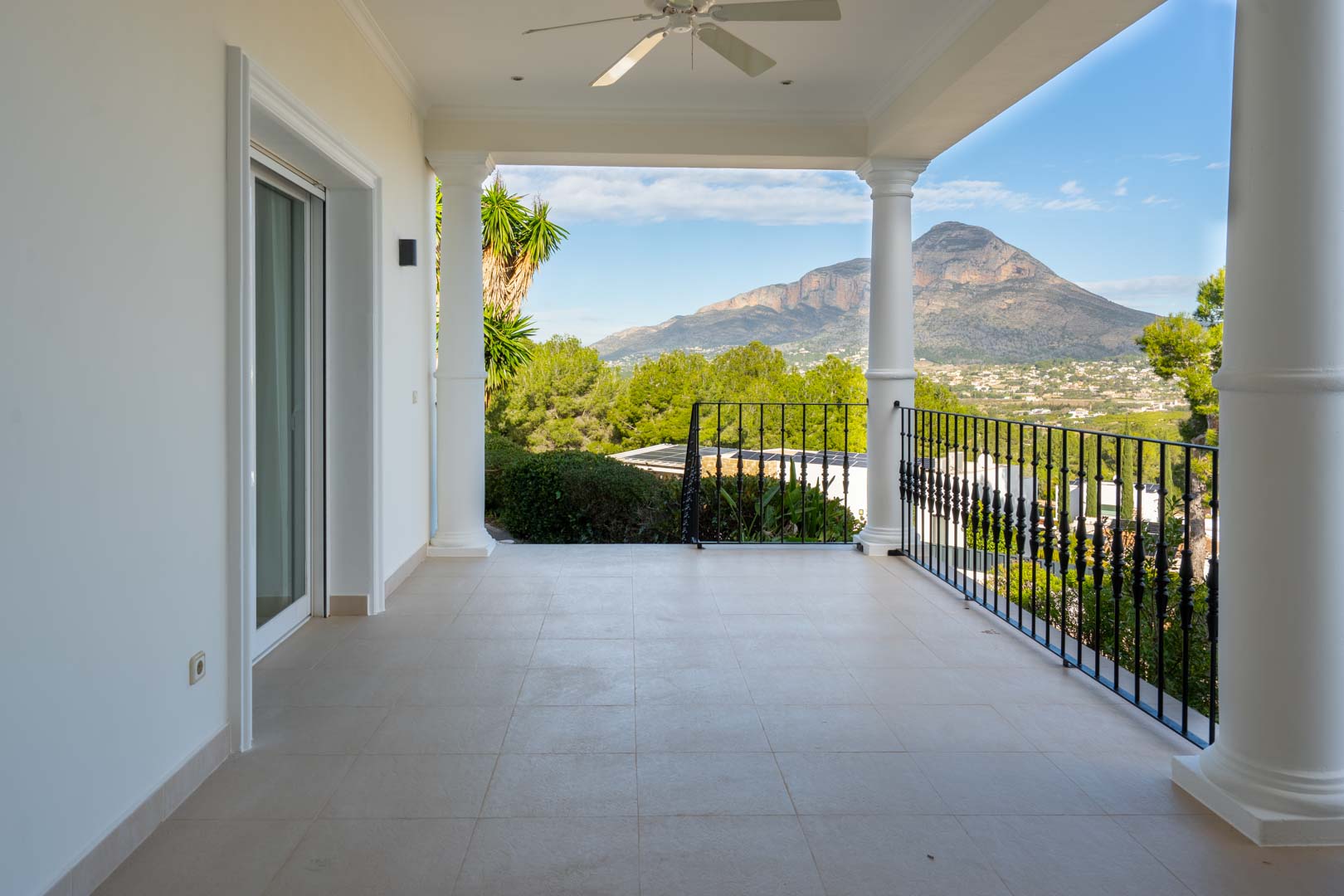 Überdachte Terrasse der Master-Suite mit klassischen Säulen, Schmiedeeisengeländer und freiem Blick auf das Montgó-Massiv und das Tal.