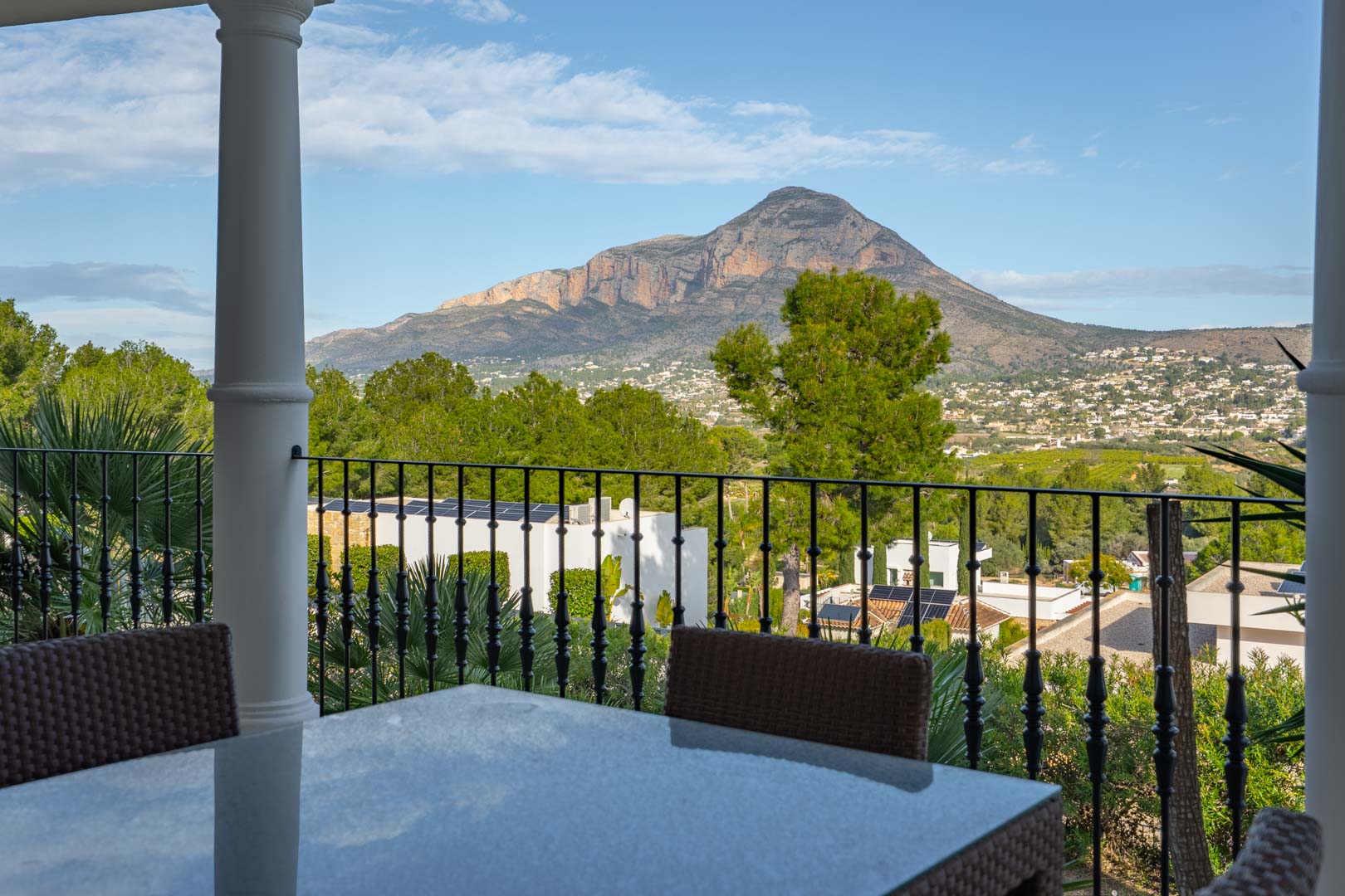 Überdachte Terrasse mit Essbereich im Freien und schmiedeeisernem Geländer, die einen freien Panoramablick auf das Montgó-Massiv bietet.