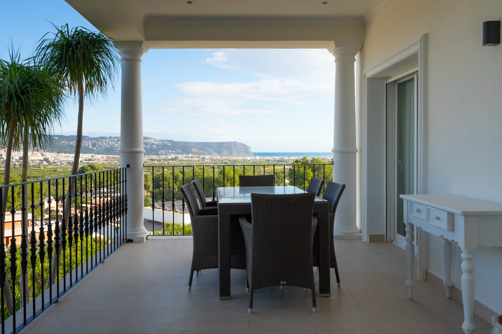 Überdachte Terrasse mit klassischen Säulen und Schmiedeeisengeländer, ausgestattet mit Essbereich und Panoramablick auf das Mittelmeer und das Tal.