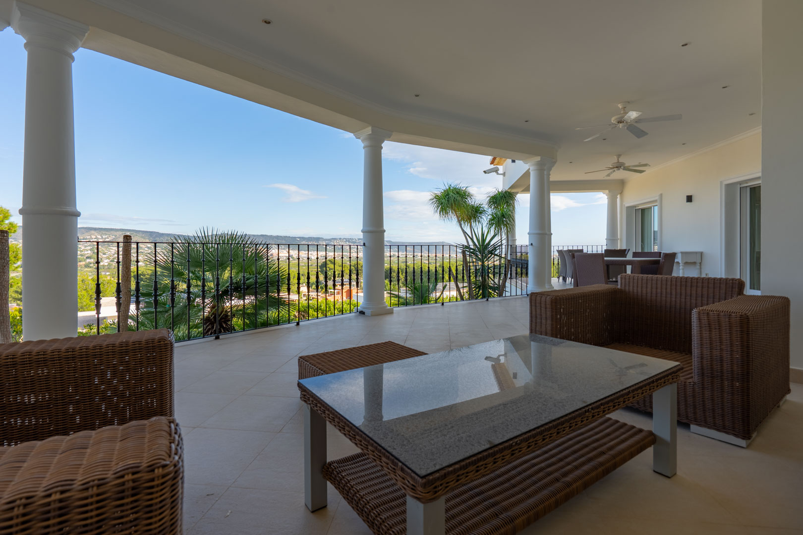 Überdachte Terrasse mit weißen Säulen, Korbmöbeln und Panoramablick auf das Tal und den Montgó. Ausgestattet mit Deckenventilatoren und Einbaustrahlern.