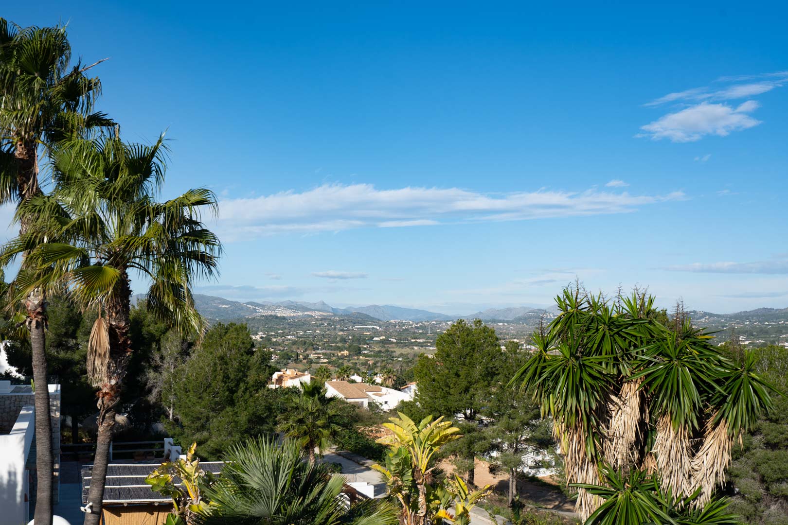 Weitläufiger Panoramablick über das Tal und die Bergketten, eingerahmt von Palmen und mediterraner Bepflanzung in einer ruhigen, erhöhten Lage.