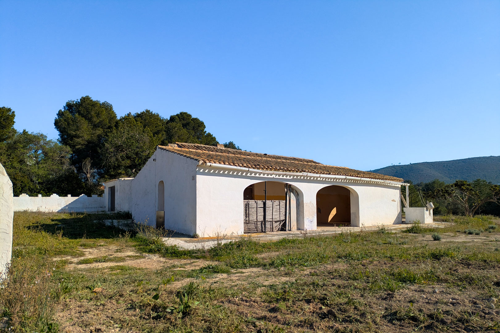 Außenansicht der traditionellen Finca mit bogenförmiger Naya und Ziegeldach auf einem weitläufigen rustikalen Grundstück mit Bergblick.