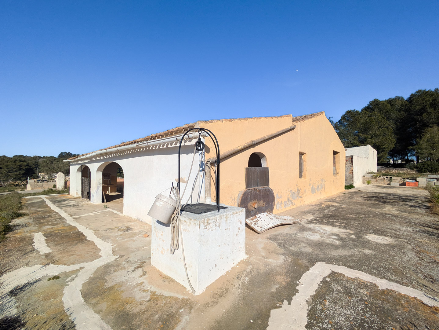 Außenansicht der traditionellen Finca mit Bogengang, antikem Brunnen im Vordergrund und weitläufiger Steinterrasse in sonniger Lage.