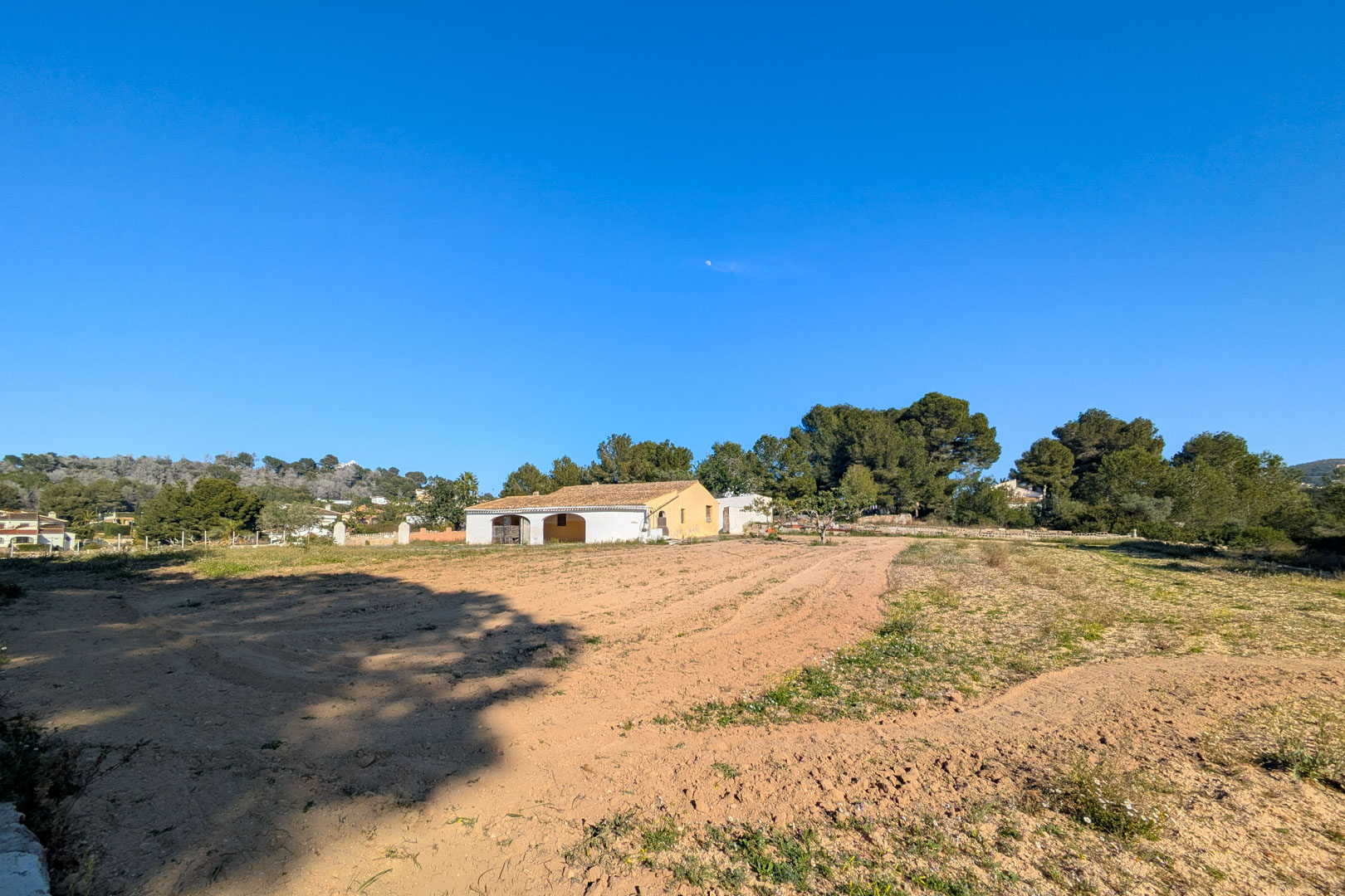 Außenansicht der traditionellen Finca mit Bogenterrasse auf einem großen, flachen rustikalen Grundstück, umgeben von Pinien und Naturlandschaft in Jávea.