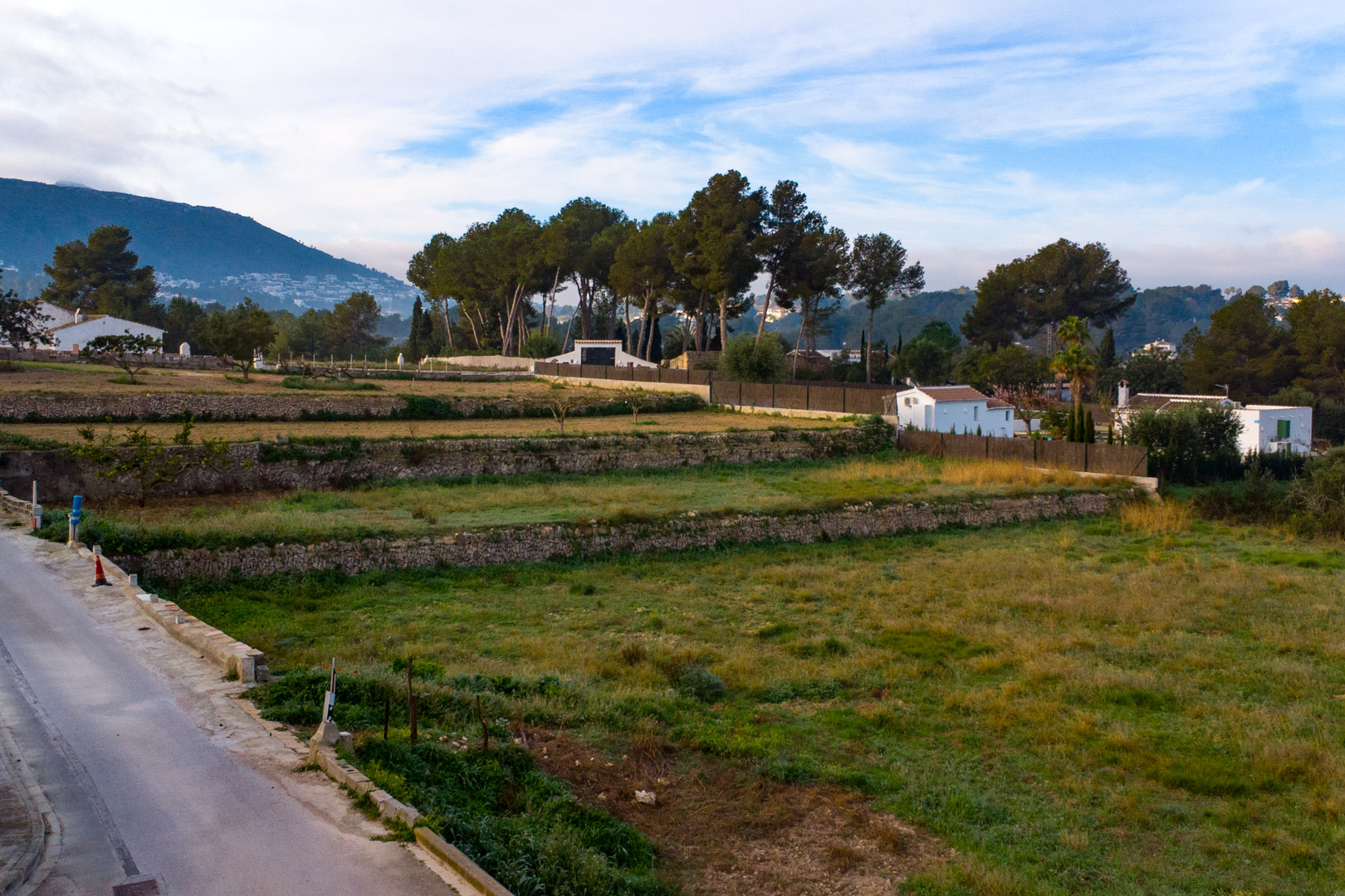 Blick auf die Trockensteinmauern des weitläufigen rustikalen Grundstücks, umgeben von mediterraner Vegetation und Bergen im Hintergrund.
