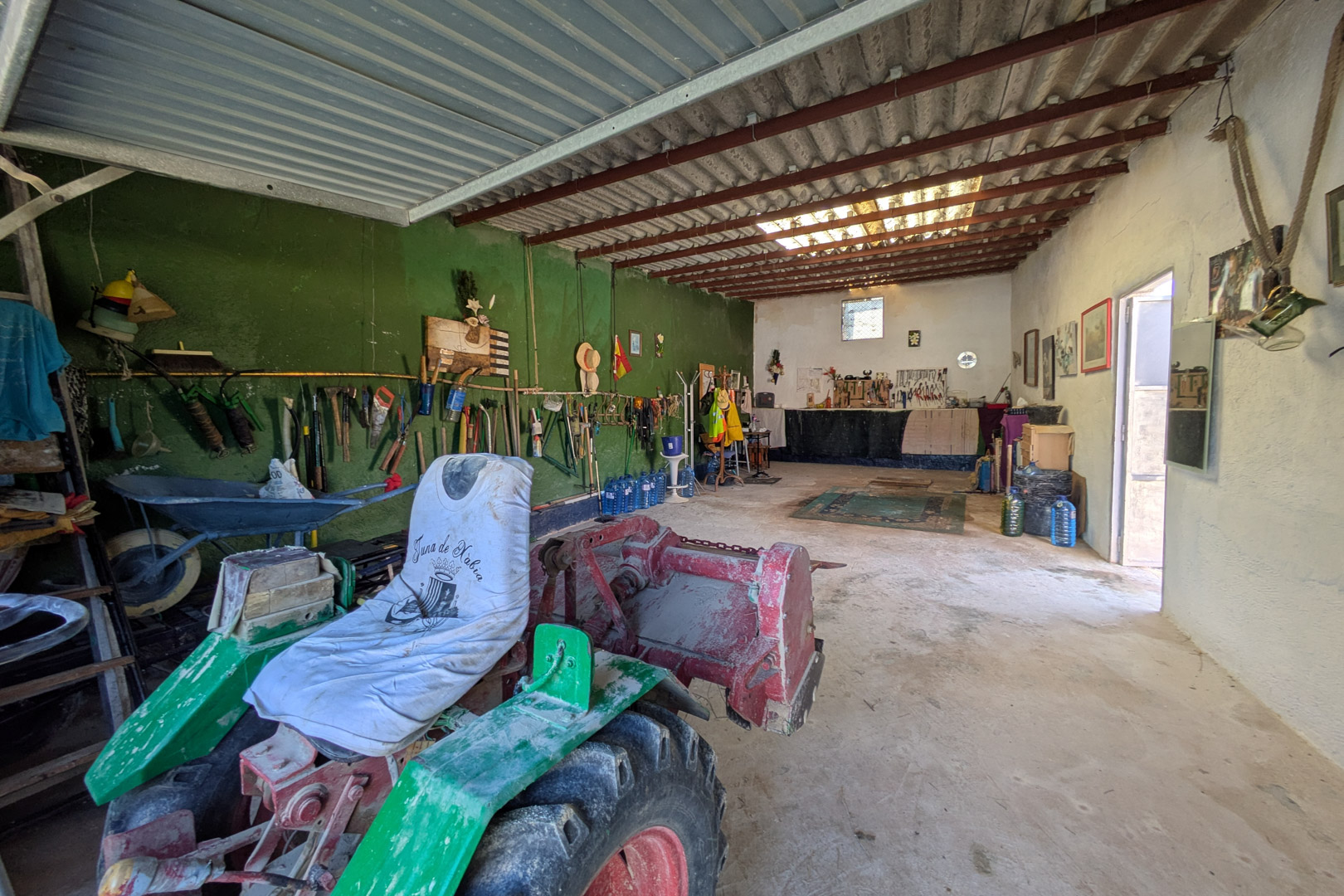 Geräumige Werkstatt oder Lagerhalle mit Betonboden und hohen Decken mit Stahlträgern, geeignet für landwirtschaftliche Maschinen und Werkzeuge.
