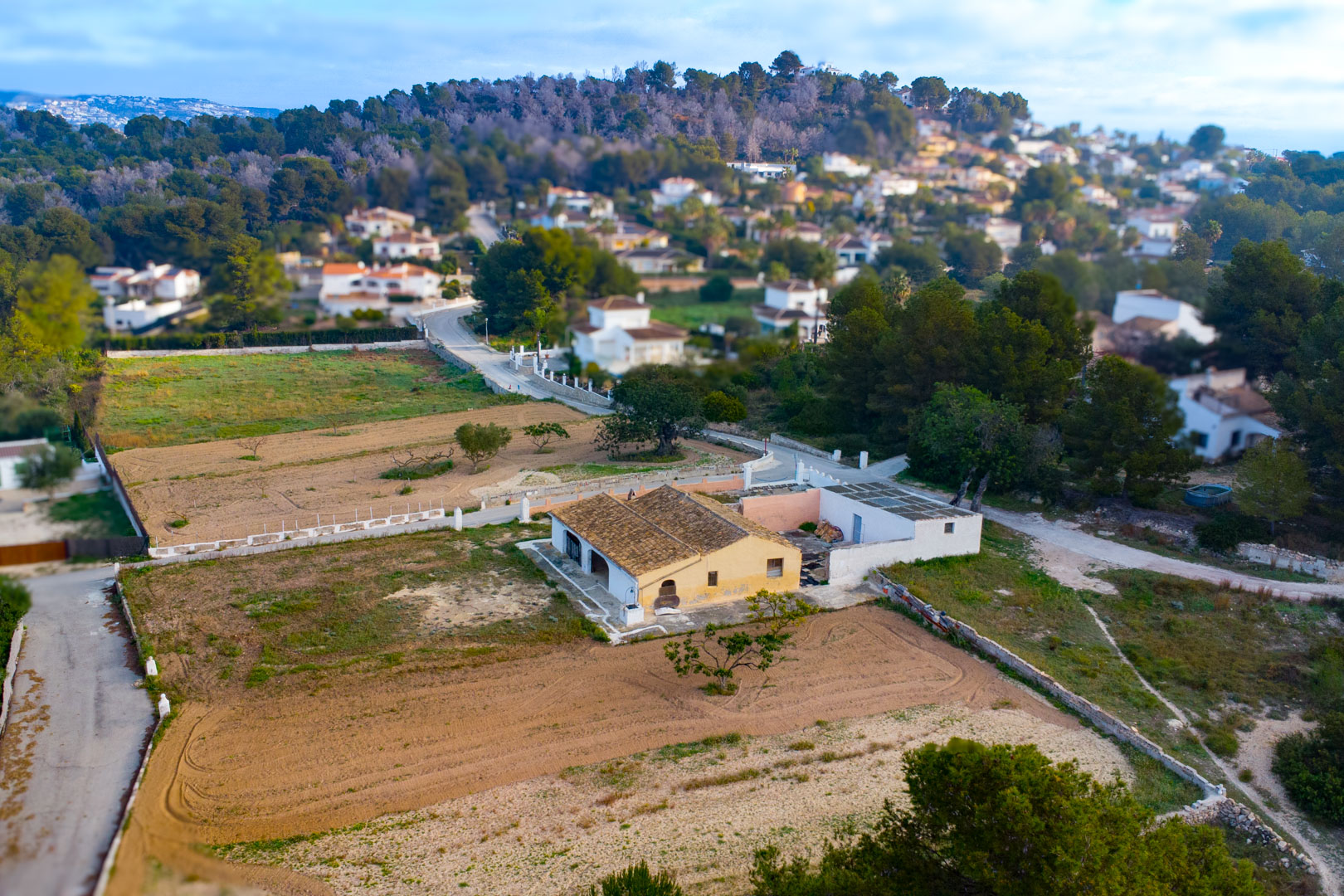 Luftaufnahme der traditionellen Finca mit Ziegeldach und ockerfarbener Fassade auf einem weitläufigen rustikalen Grundstück, umgeben von Natur.