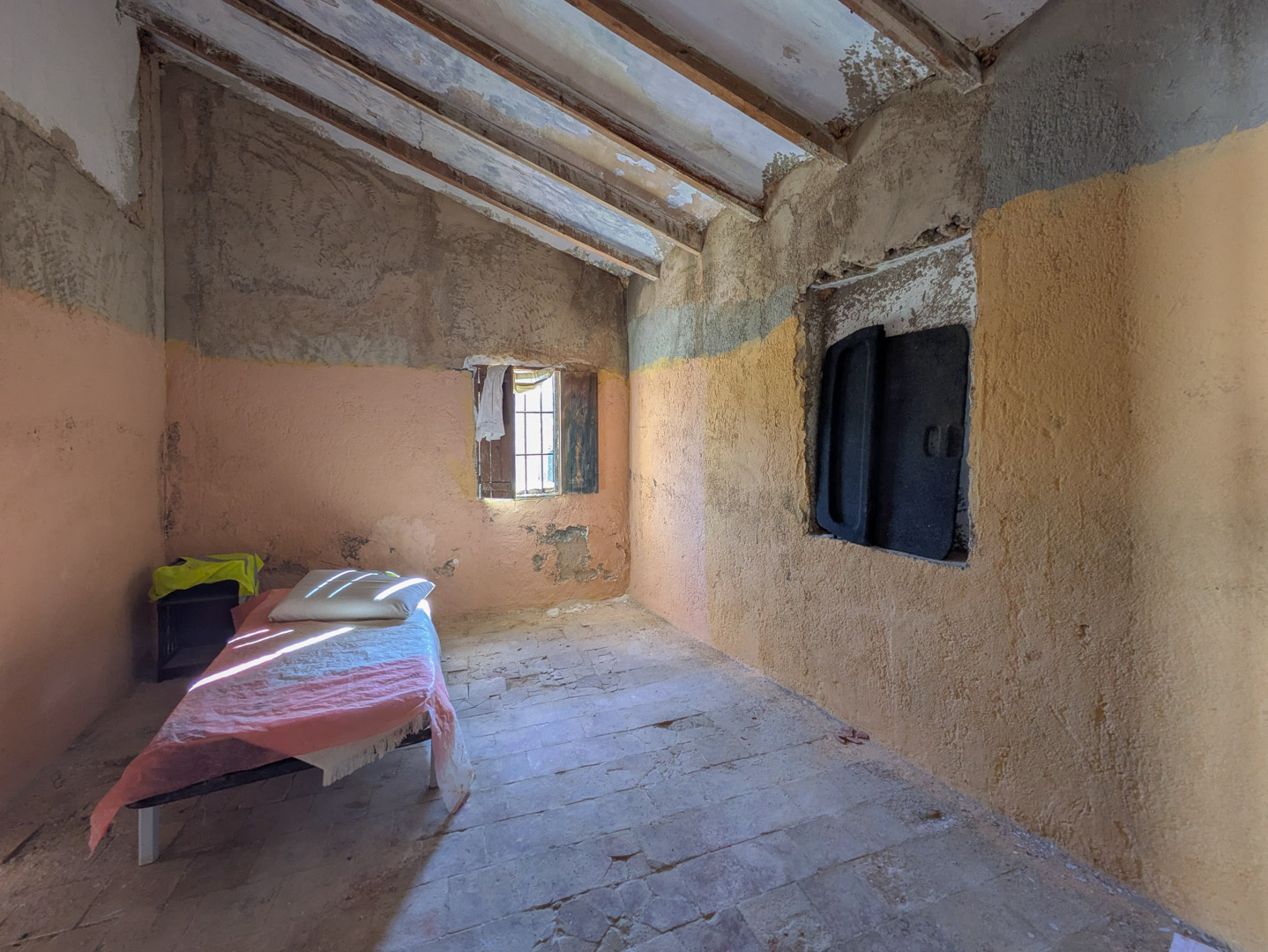Rustikaler Innenraum mit sichtbaren Holzbalken, originalen Terrakottaböden und renovierungsbedürftigen Wänden mit natürlichem Lichteinfall.