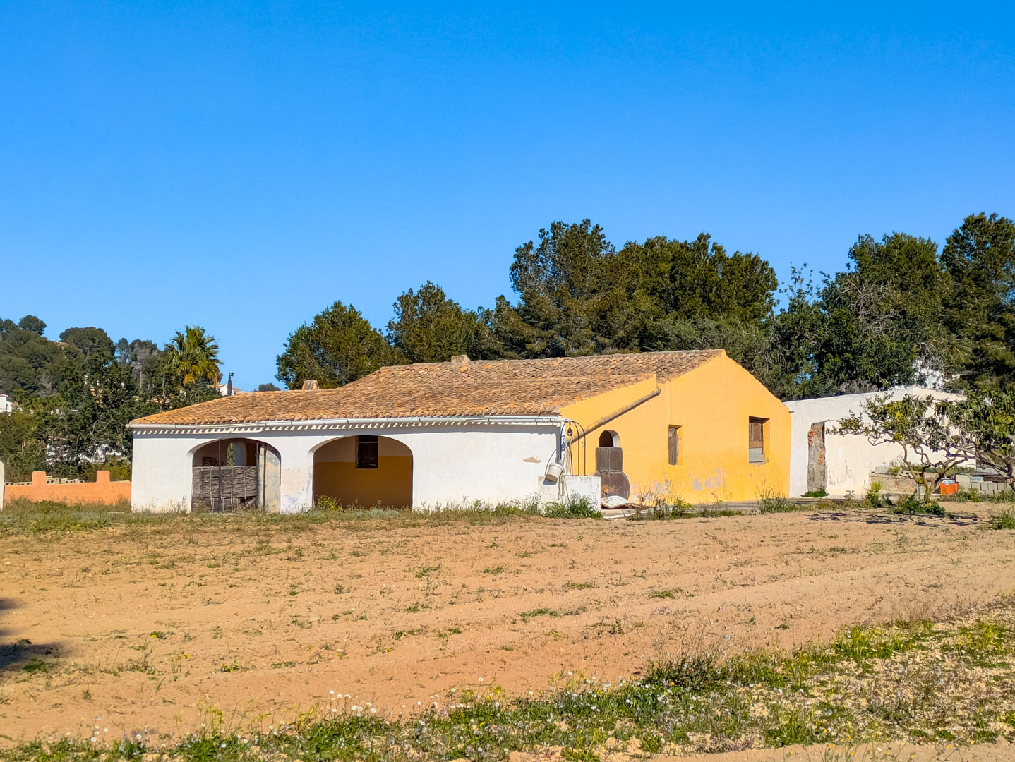 Traditionelle Finca-Fassade mit Rundbogen-Veranda und Ziegeldach auf einem weitläufigen rustikalen Grundstück, umgeben von Pinienwäldern.
