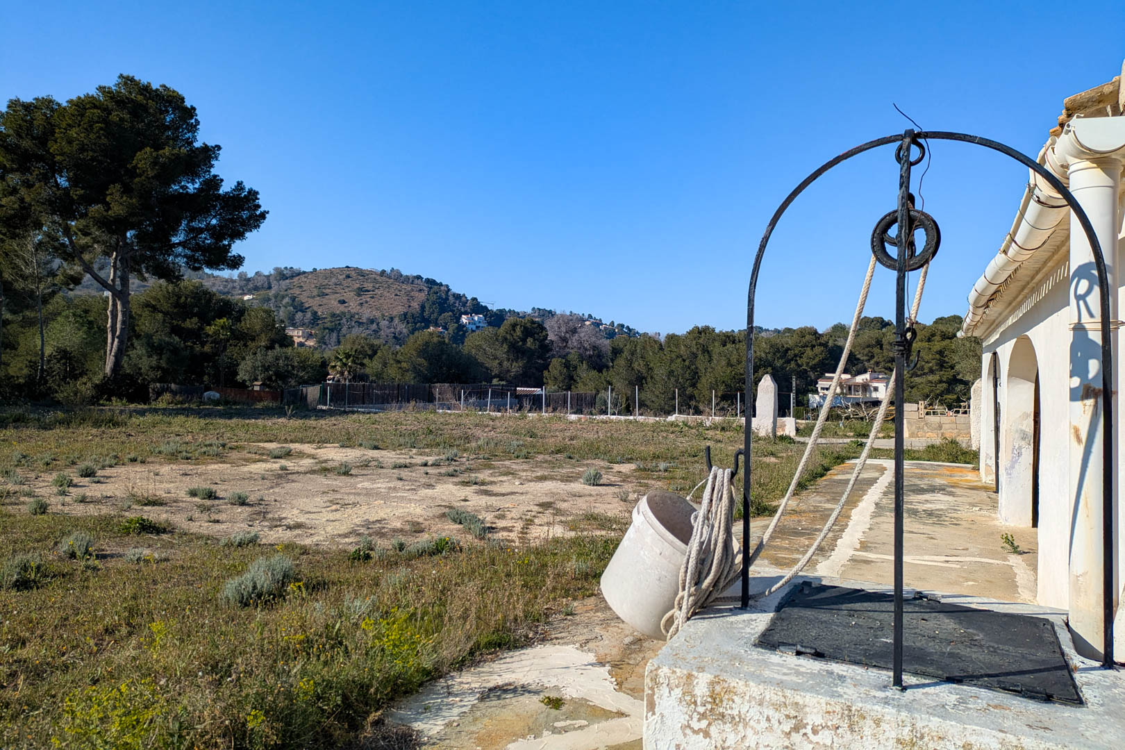 Traditioneller Brunnen mit Eisenbogen und Seilzug auf dem weitläufigen rustikalen Grundstück, mit Blick auf die umliegenden Hügel und die Landschaft.