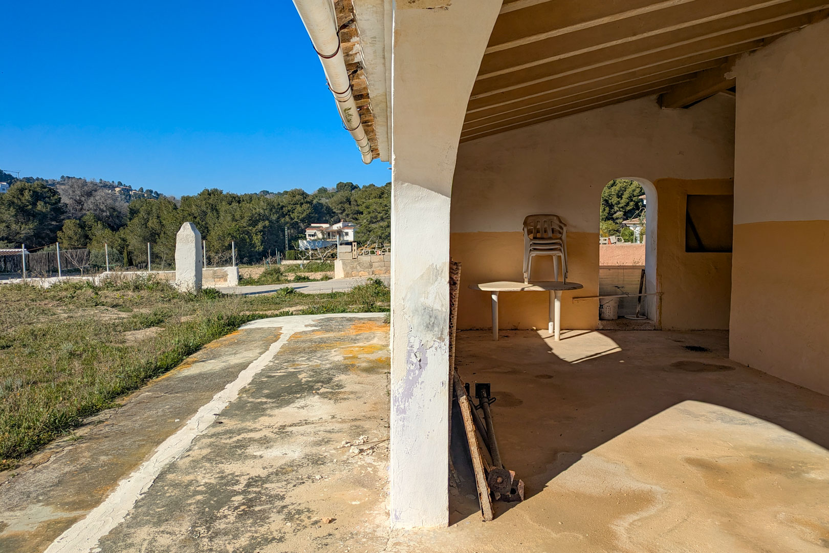 Überdachte Veranda mit sichtbaren Holzbalken und Rundbogenpfeilern, die einen Blick auf das weitläufige rustikale Grundstück bietet.