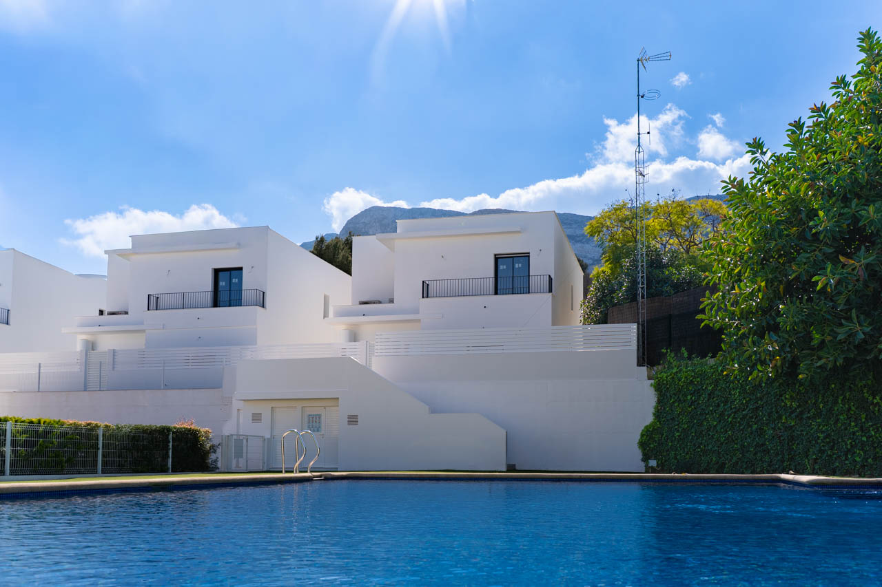 Blick auf die modernen Villen vom Gemeinschaftspool aus, mit weißen minimalistischen Fassaden und dem Montgó-Massiv im Hintergrund.