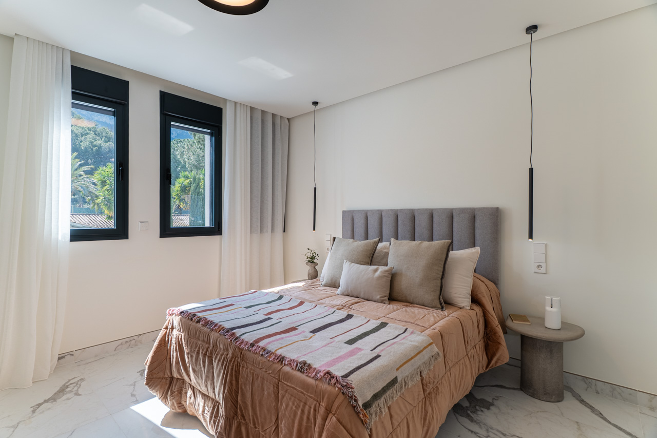 Doppelzimmer mit Feinsteinzeugboden in Marmoroptik, grau gepolstertem Kopfteil und schwarz gerahmten Fenstern, die den Blick ins Grüne freigeben.