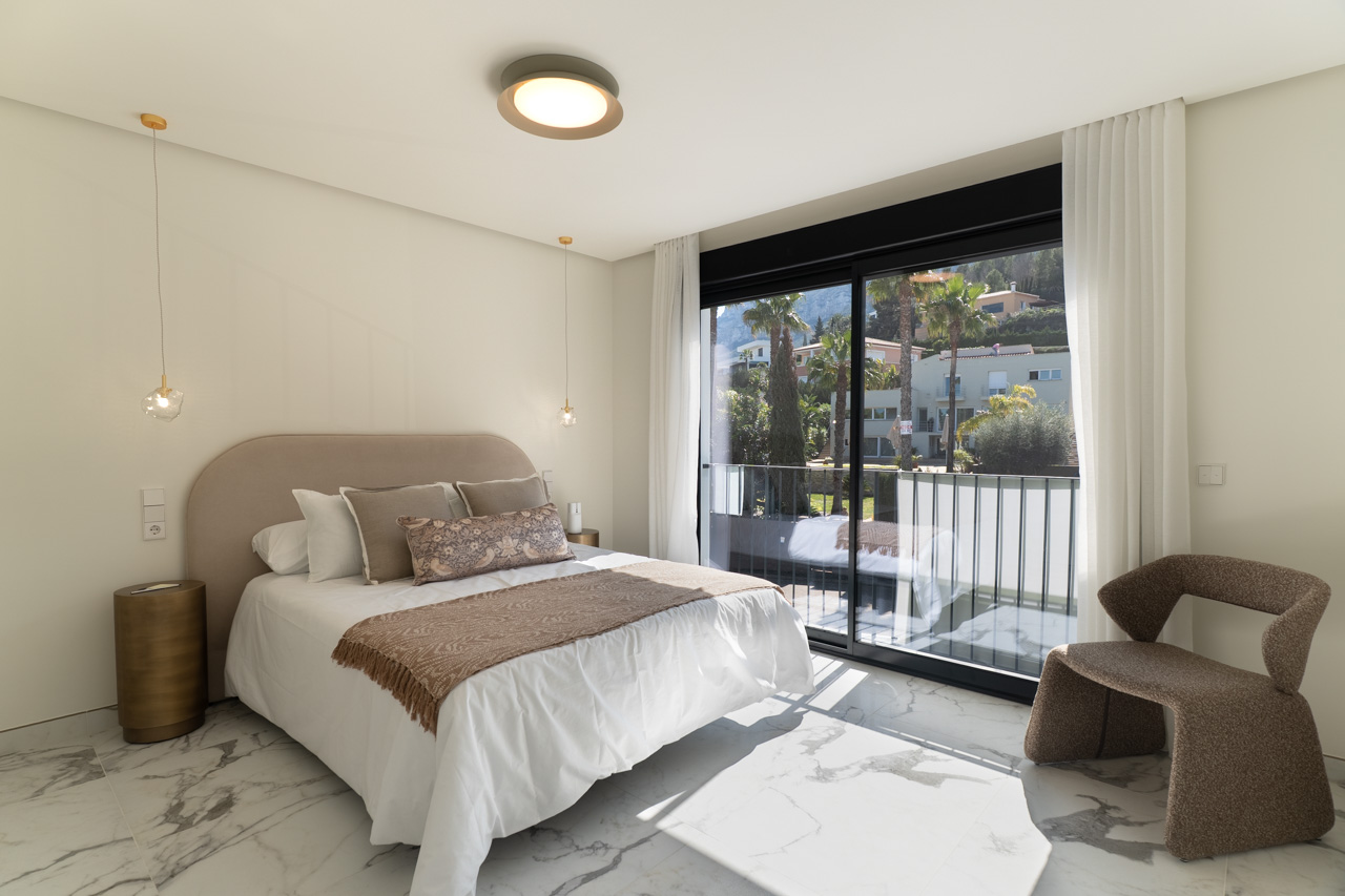 Hauptschlafzimmer mit Feinsteinzeugboden in Marmoroptik und bodentiefen Glasschiebetüren, die auf einen privaten Balkon mit Ausblick führen.