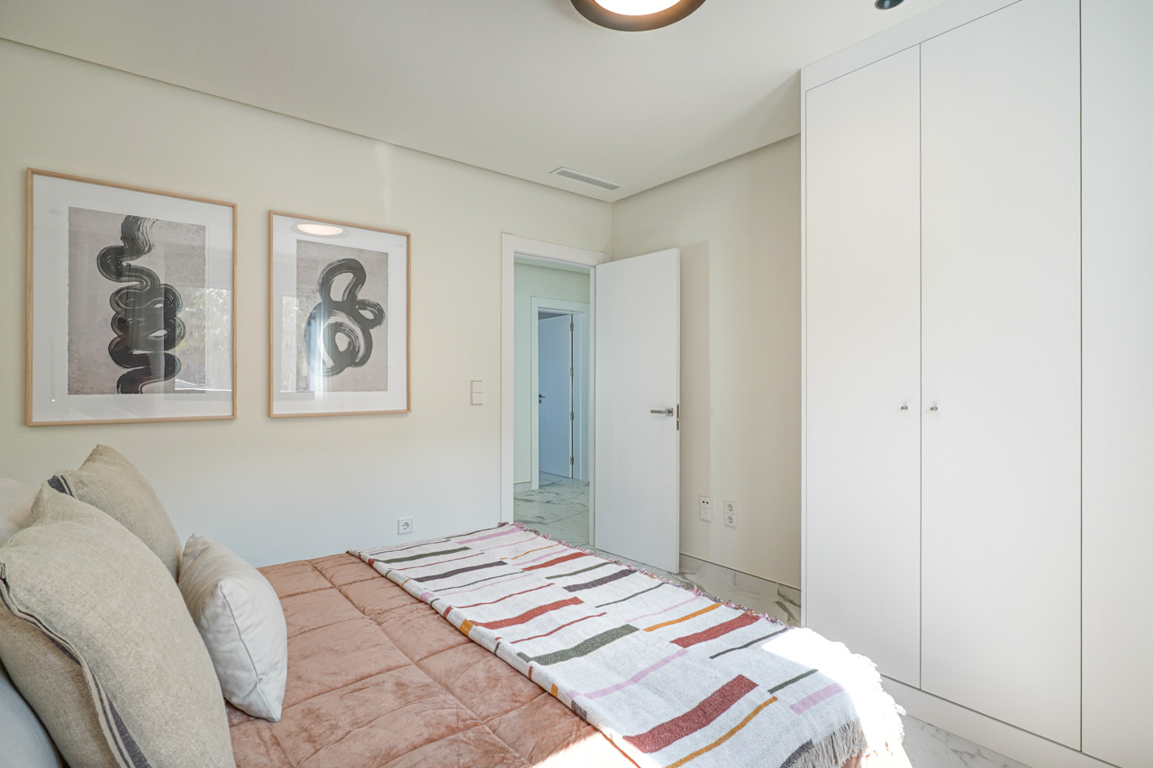 Helles Schlafzimmer mit deckenhohen weißen Einbauschränken, Feinsteinzeugboden in Marmoroptik und minimalistischer Wanddekoration.