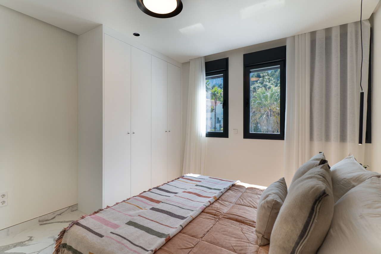Helles Schlafzimmer mit raumhohen weißen Einbauschränken, Marmorboden und Fenstern mit Blick auf die mediterrane Umgebung.