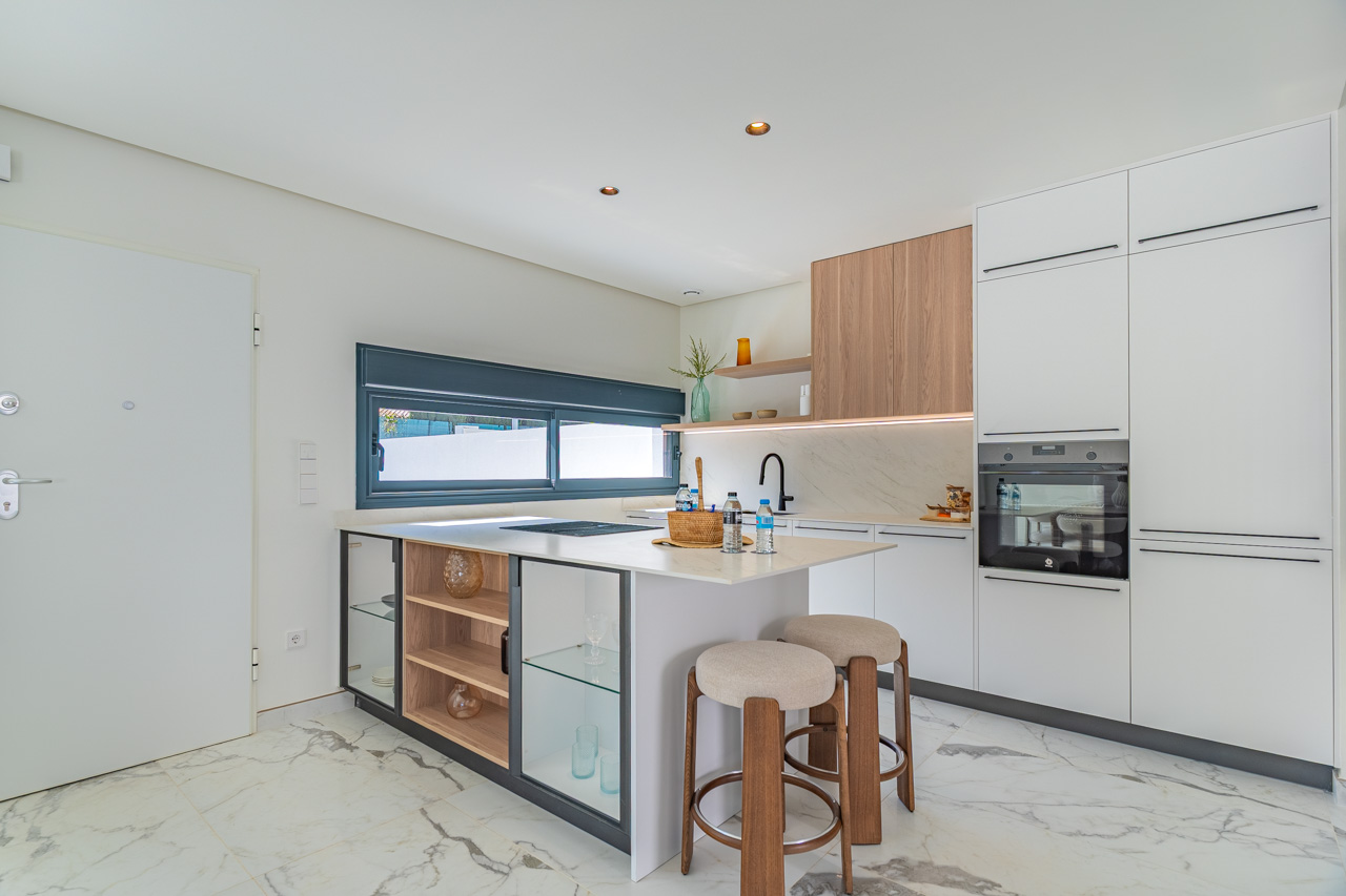 Moderne offene Küche mit Kochinsel, weißen Schränken und Holzelementen. Ausgestattet mit integrierten Geräten und Feinsteinzeugböden in Marmoroptik.