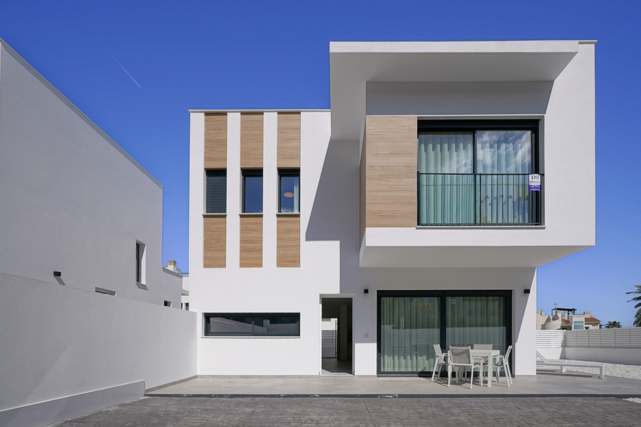 Moderne Villenfassade mit weißen Wänden, Holzoptik-Elementen, einer großzügigen Erdgeschoss-Terrasse und einem auskragenden Obergeschoss mit Balkon.