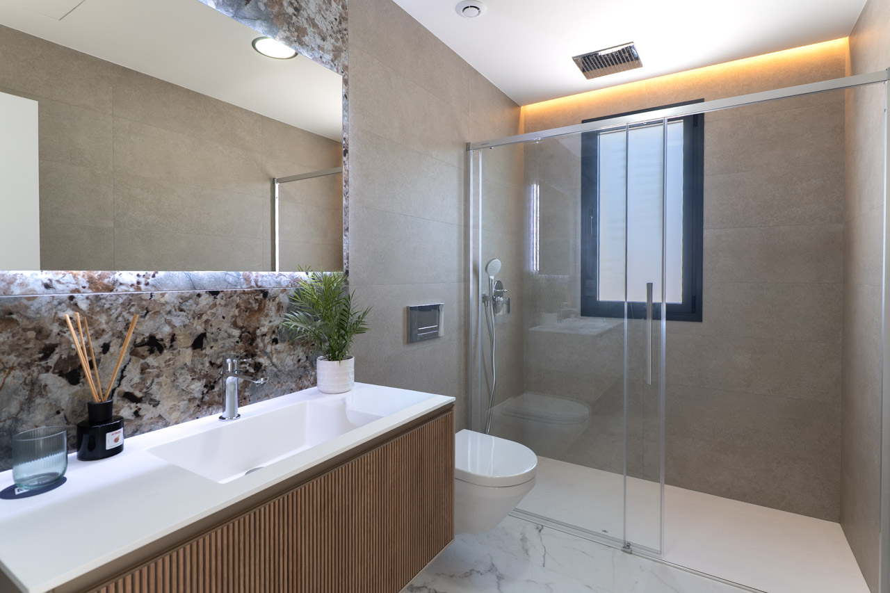 Modernes Badezimmer mit Waschtisch aus Holzlamellen, Marmor-Rückwand und ebenerdiger Dusche mit Glastrennwand und indirekter Beleuchtung.
