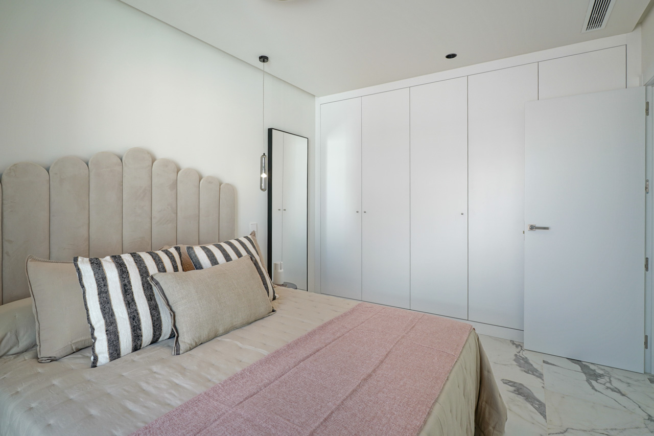 Modernes Schlafzimmer mit raumhohen weißen Einbauschränken, Marmorboden und einem dekorativ geschwungenen Polsterkopfteil mit minimalistischer Pendelleuchte.