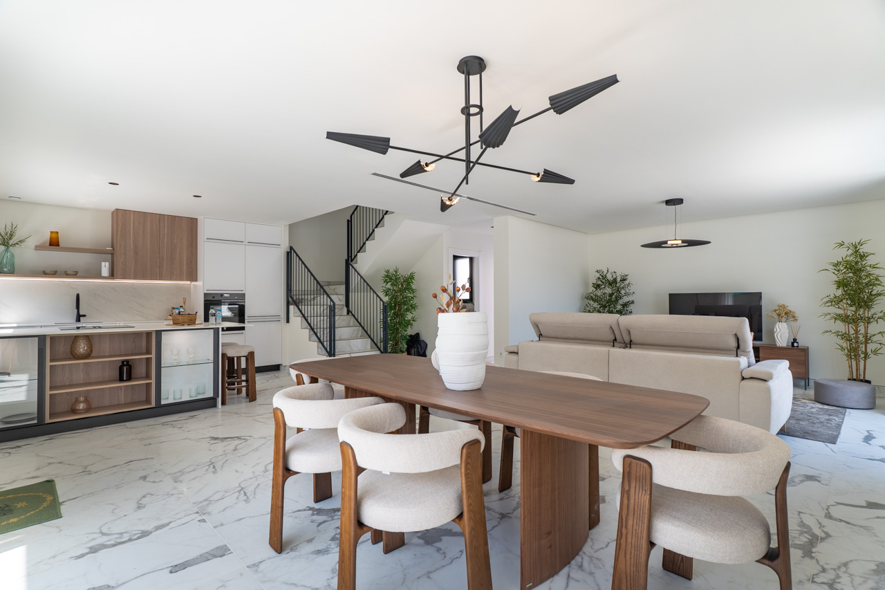 Offener Wohn- und Essbereich mit modernem Küchendesign, Marmoreffekt-Fliesen und einer markanten schwarzen Designerleuchte über dem Holztisch.
