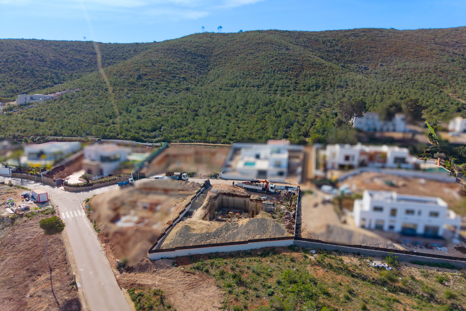 Luftaufnahme des Grundstücks während der Bauphase mit Fokus auf den Erdaushub für das Kellergeschoss und das Fundament in einer ruhigen, naturnahen Wohngegend.