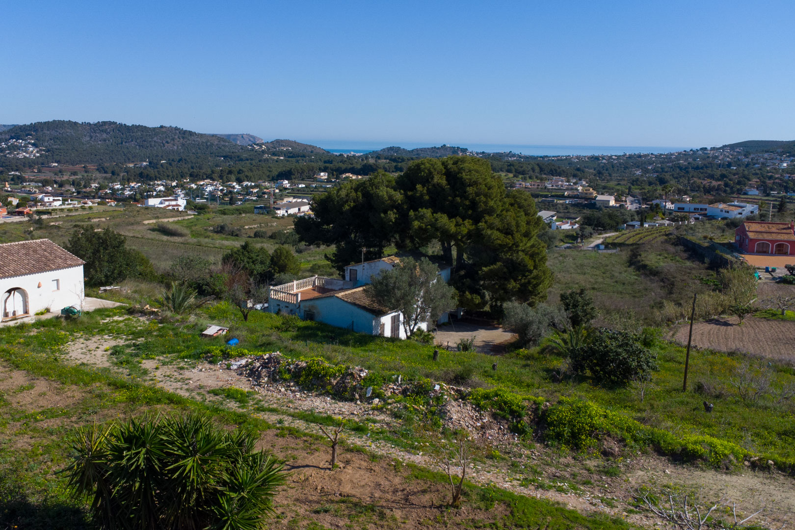 Erhöhte Ansicht der traditionellen Finca und des rustikalen Grundstücks mit Panoramablick über das Tal von Benitachell bis hin zum Mittelmeer.