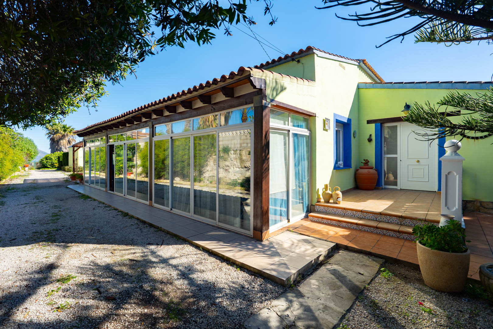 Finca-Außenansicht mit verglaster Naya, Holzbalken und einem gefliesten Eingangsbereich mit mediterranen blauen Akzenten.