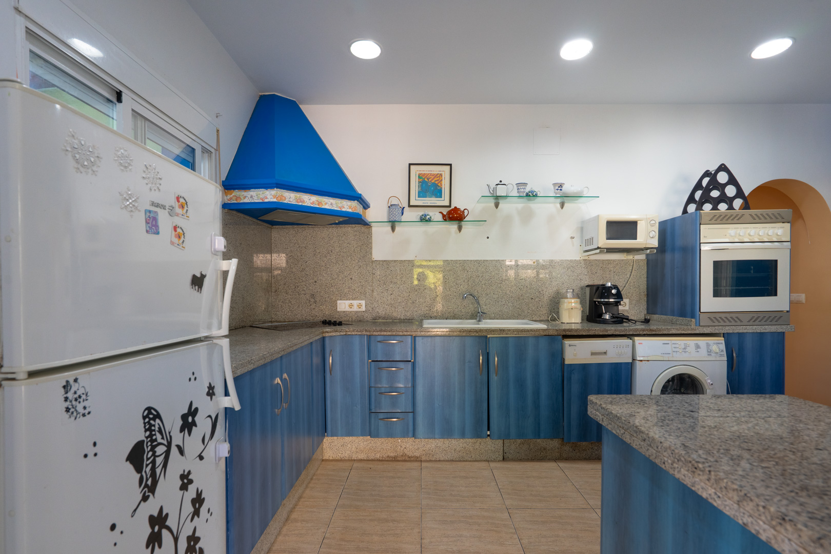 Funktionale Küche mit blauen Fronten, Arbeitsplatten aus grauem Granit und passendem Spritzschutz. Ausgestattet mit blauer Dunstabzugshaube und Einbaugeräten.