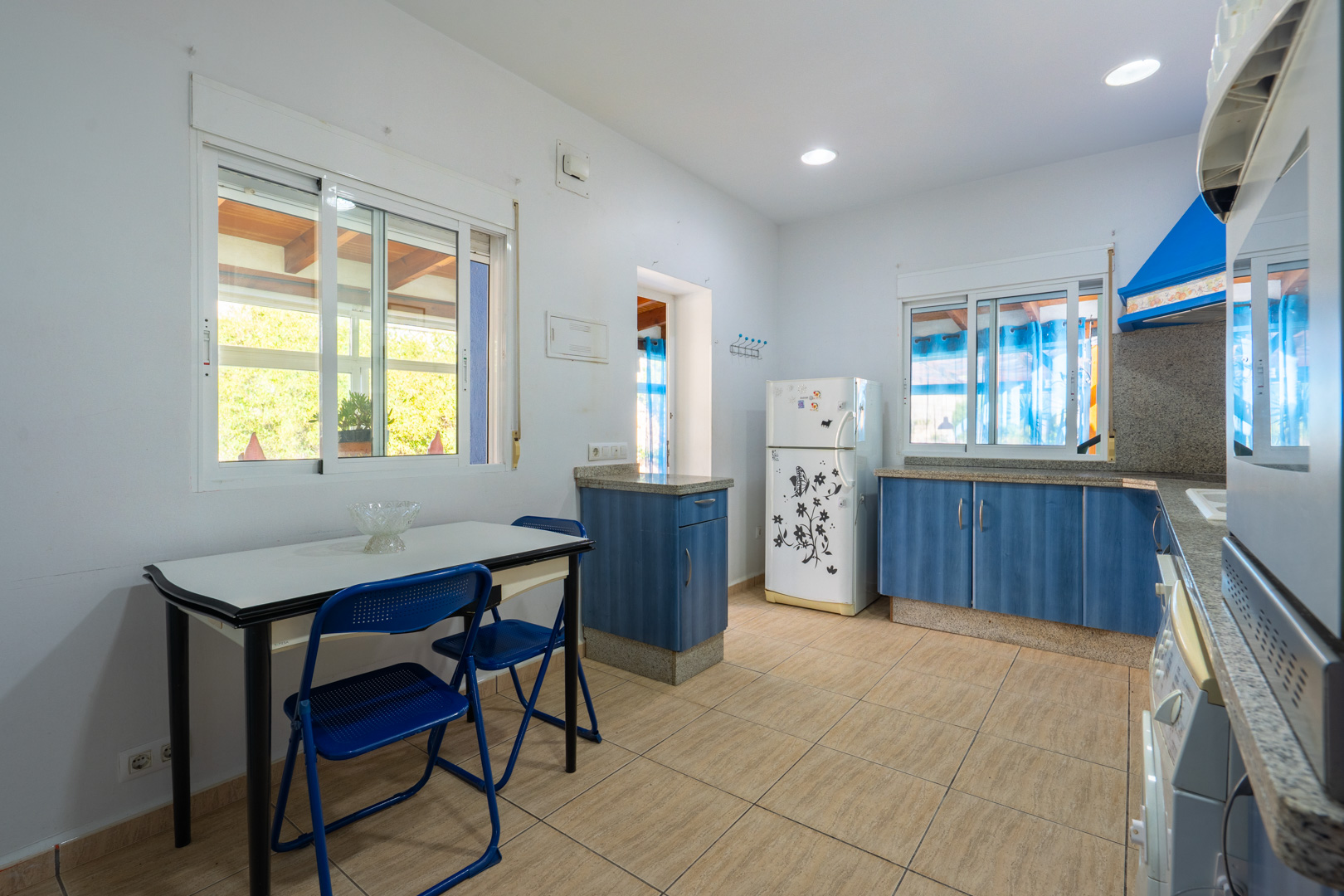 Funktionale Küche mit blauen Schränken, Granitarbeitsplatten und einem Essbereich. Sie ist mit Einbaustrahlern und Fenstern mit Blick auf die Veranda ausgestattet.