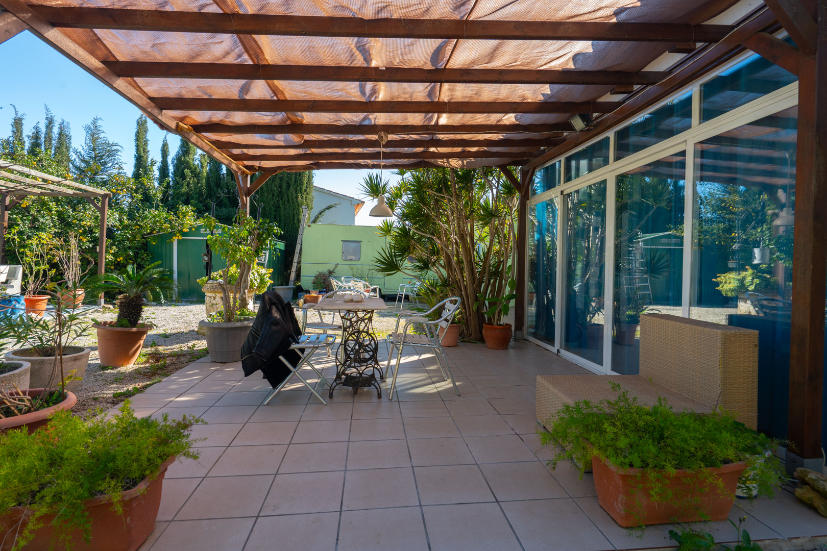 Geflieste Terrasse mit Holzpergola und Schattenspender, ausgestattet mit Gartenmöbeln und Topfpflanzen angrenzend an den Gartenbereich.
