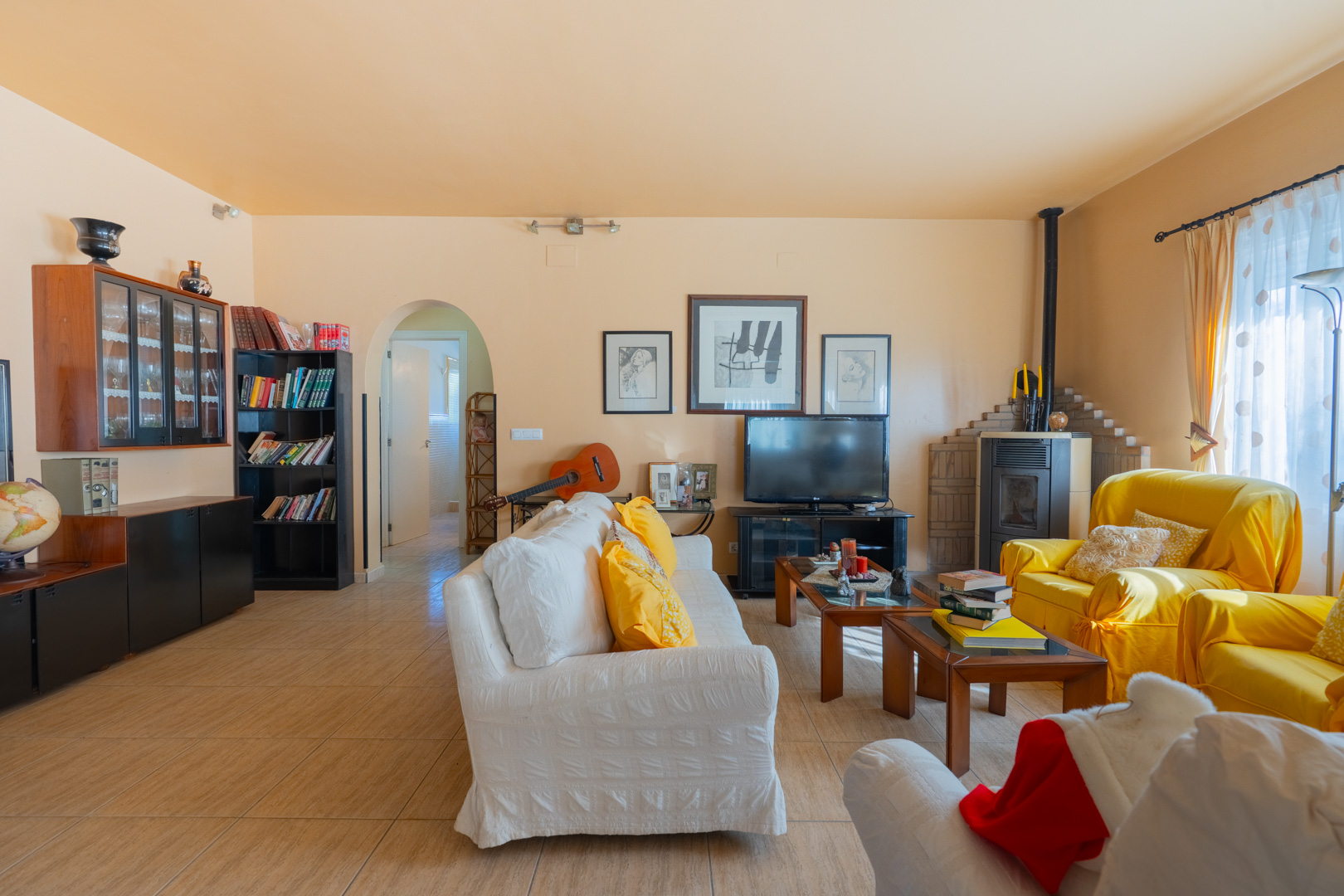 Großzügiges Wohnzimmer im traditionellen Stil mit Holzofen, Fliesenboden und einem Rundbogen-Durchgang zu den weiteren Räumen.