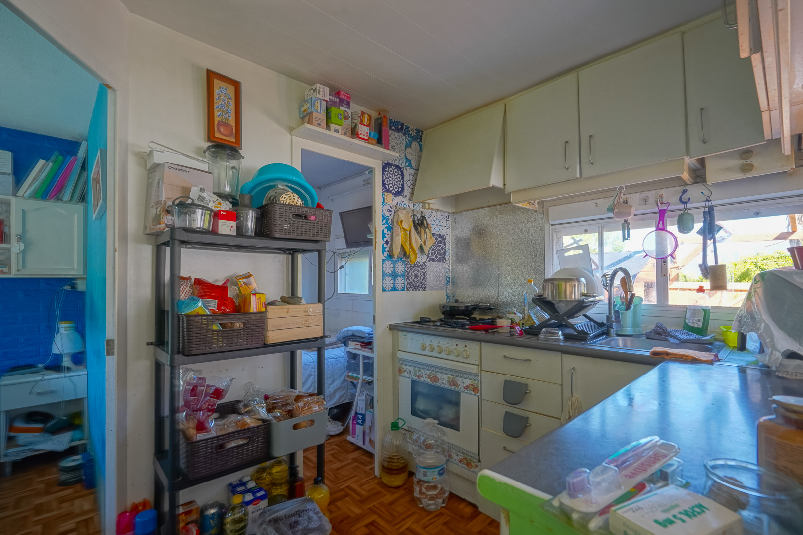 Kompakte Küche im Gästehaus mit weißen Schränken, dekorativem Fliesenspiegel und praktischen Lagerregalen, ergänzt durch natürliches Licht vom Fenster.