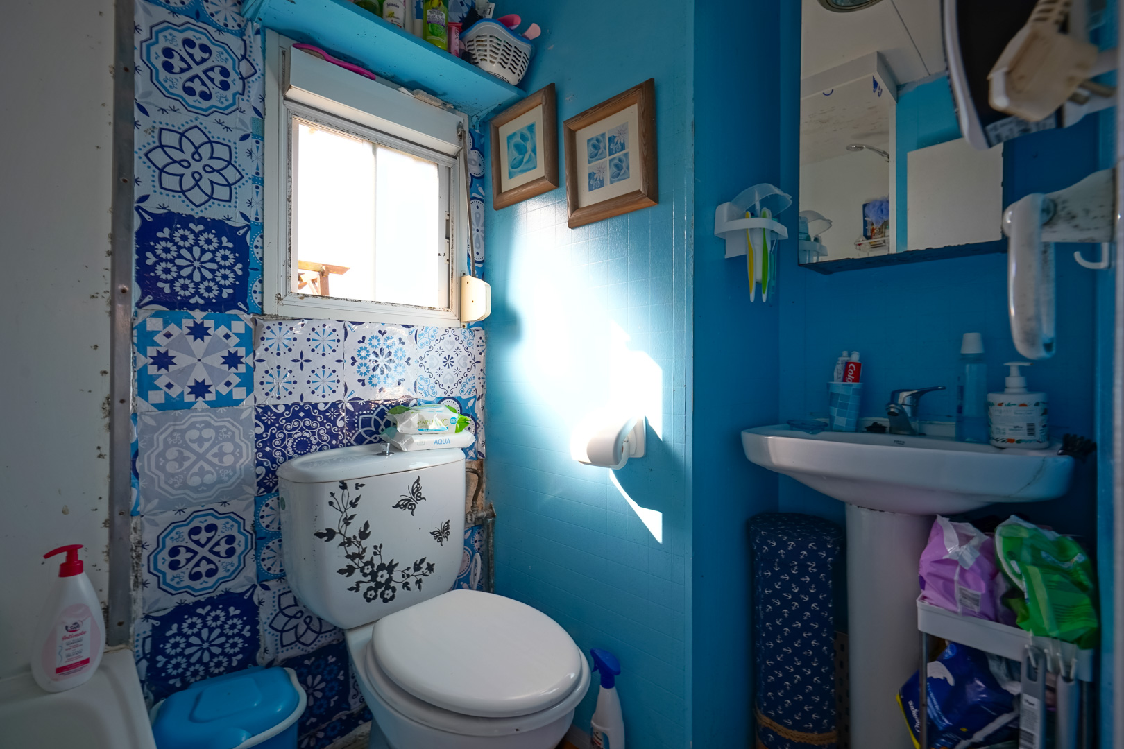 Kompaktes Badezimmer mit blauen Wänden, dekorativen gemusterten Fliesen, einem Standwaschbecken und natürlichem Lichteinfall durch das Fenster.