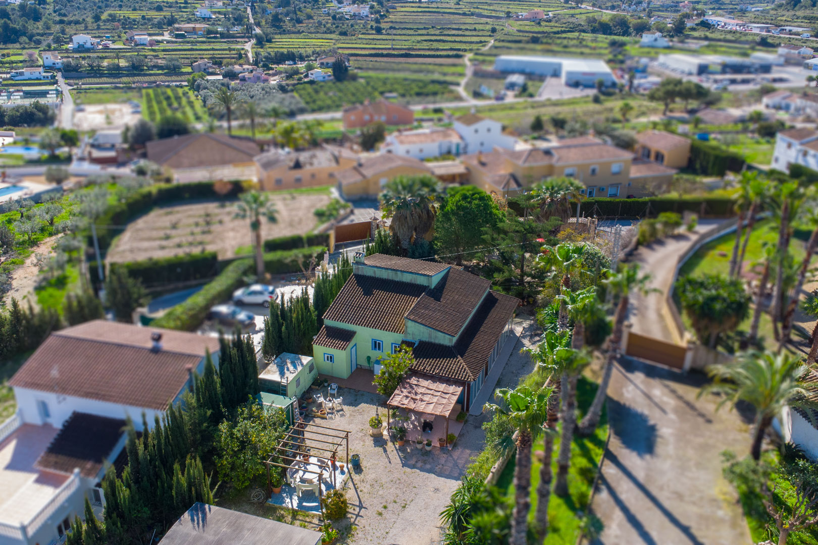 Luftaufnahme der traditionellen Finca mit grüner Fassade, Ziegeldach und Außenbereichen mit Holzpergolen, umgeben von Palmen und ländlicher Umgebung.