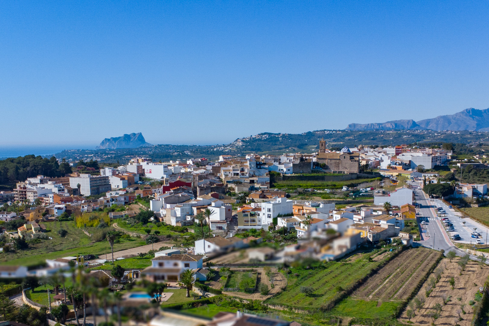 Panorama-Luftaufnahme von Benitachell mit Blick auf das historische Zentrum, die Kirche und den Peñón de Ifach am Mittelmeerhorizont.
