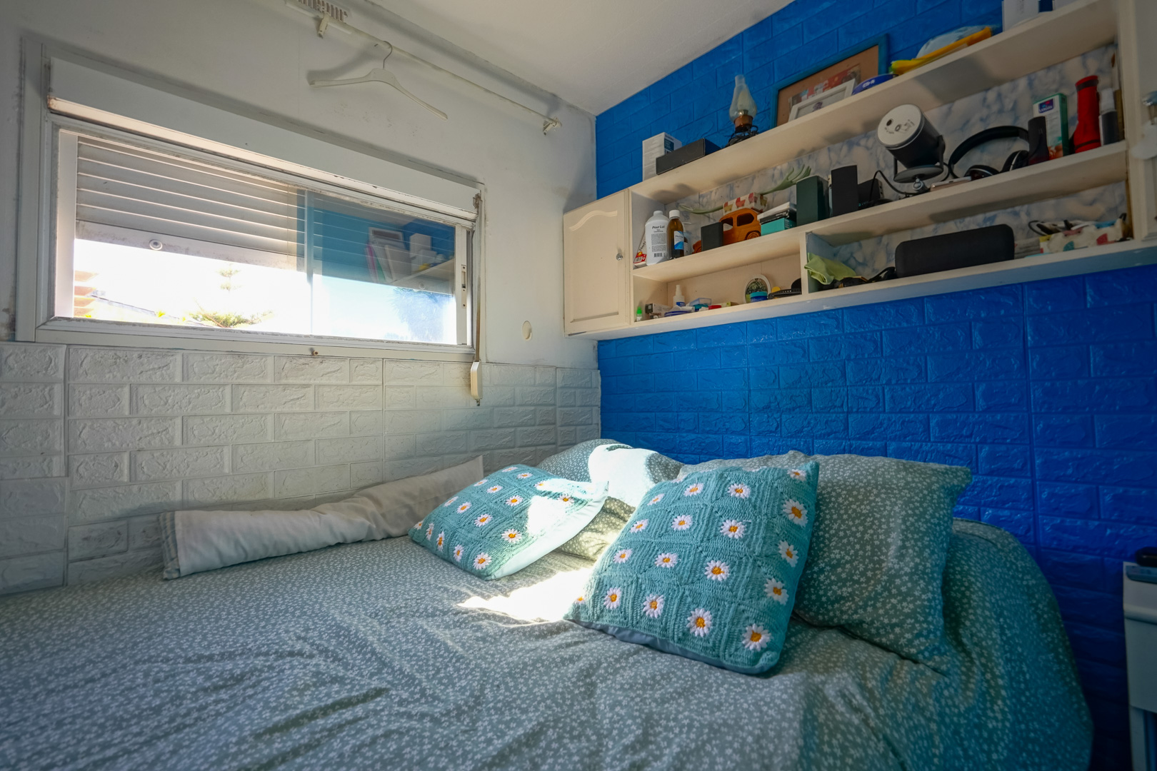 Schlafzimmer in der Fertighauseinheit mit blau-weißen Wänden in Backsteinoptik, integrierten Regalen und natürlichem Licht.
