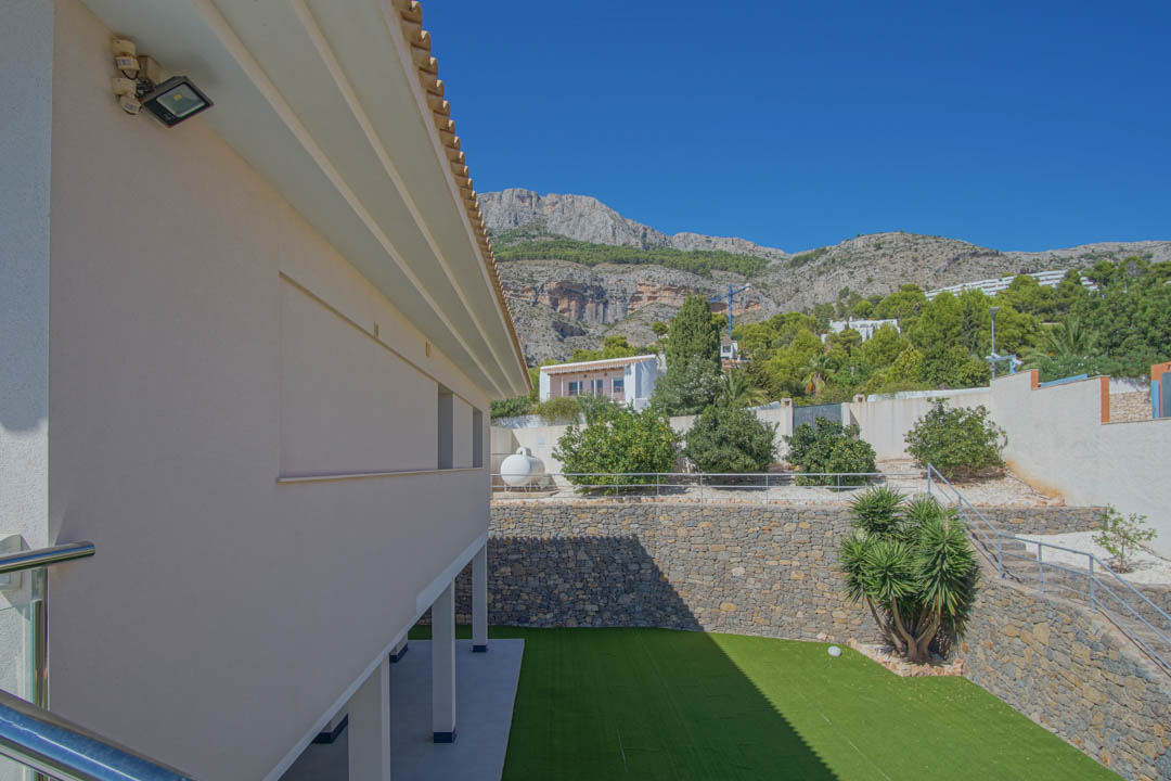 Außenansicht des unteren Gartens mit Kunstrasen, Natursteinmauern und Metalltreppen vor der Kulisse der Berge der Sierra de Altea.