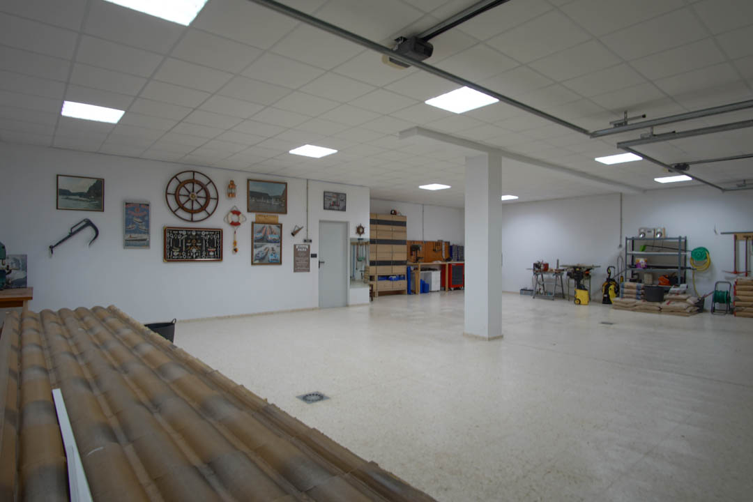 Großzügige Garage für fünf Fahrzeuge mit LED-Panel-Beleuchtung, integriertem Werkstattbereich und maritimer Wanddekoration auf hellem Fliesenboden.