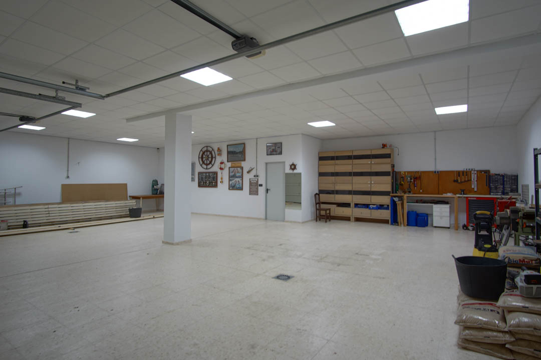 Großzügige Garage für mehrere Fahrzeuge mit integriertem Werkstattbereich, LED-Deckenbeleuchtung und funktionalen Lagersystemen.