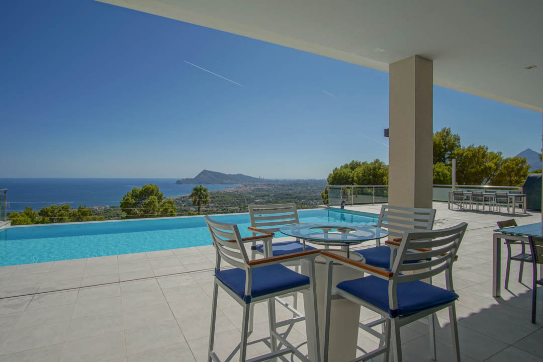 Großzügige Terrasse mit Infinity-Pool und Panoramablick auf das Mittelmeer. Ausgestattet mit modernen Barhockern und hellen Bodenfliesen.
