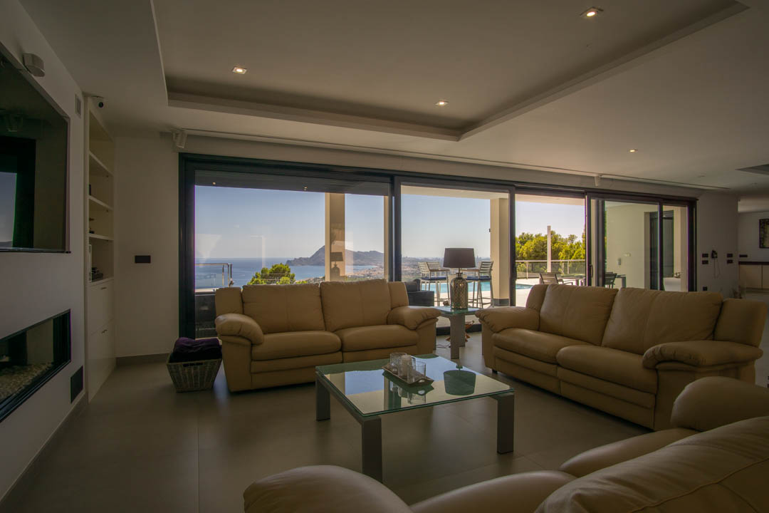 Großzügiger Wohnbereich mit Ledersofas, Deckeneinbaustrahlern und bodentiefen Glasfronten mit Panoramablick auf das Meer und die Bucht von Altea.